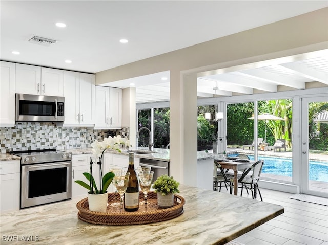 kitchen featuring white cabinets, light stone counters, appliances with stainless steel finishes, and tasteful backsplash