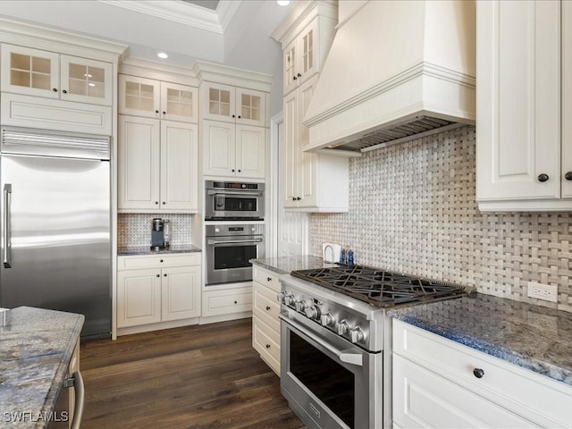 kitchen featuring dark stone countertops, white cabinets, custom range hood, and premium appliances