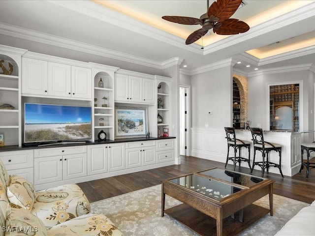 living room with a raised ceiling, ceiling fan, dark hardwood / wood-style flooring, and crown molding