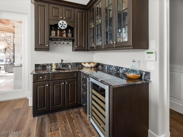 bar featuring dark brown cabinetry, beverage cooler, and dark stone counters