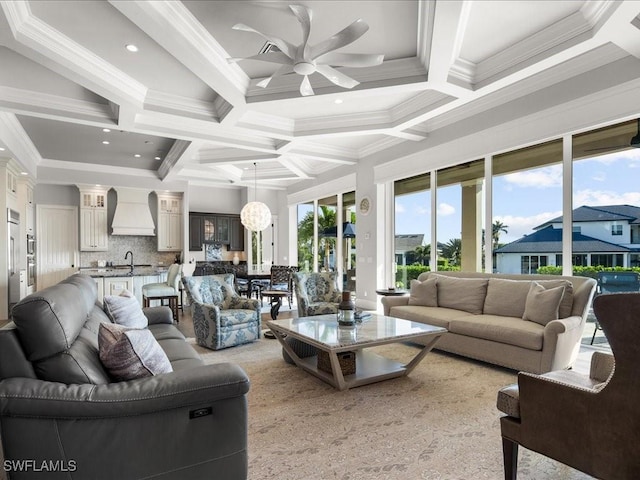 living room featuring coffered ceiling, ceiling fan with notable chandelier, crown molding, sink, and beam ceiling