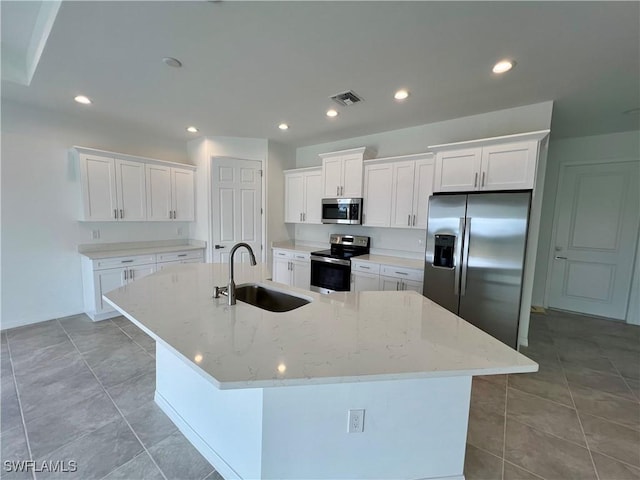 kitchen with a large island with sink, sink, light stone countertops, appliances with stainless steel finishes, and white cabinetry