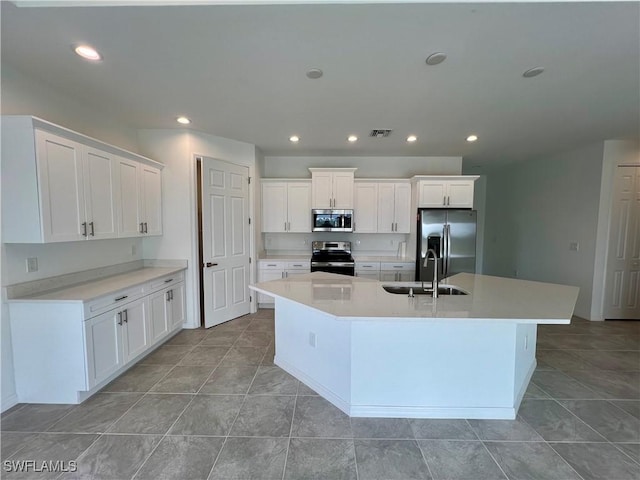 kitchen featuring white cabinets, sink, stainless steel appliances, and an island with sink