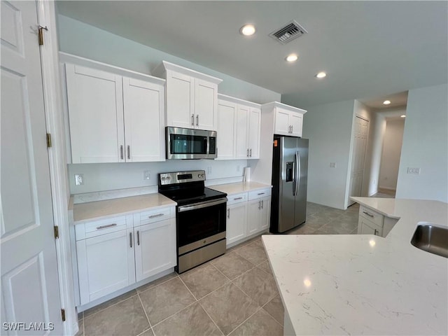 kitchen featuring light tile patterned floors, stainless steel appliances, white cabinetry, and light stone counters