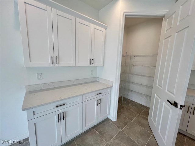 interior space with light stone countertops, tile patterned flooring, and white cabinetry