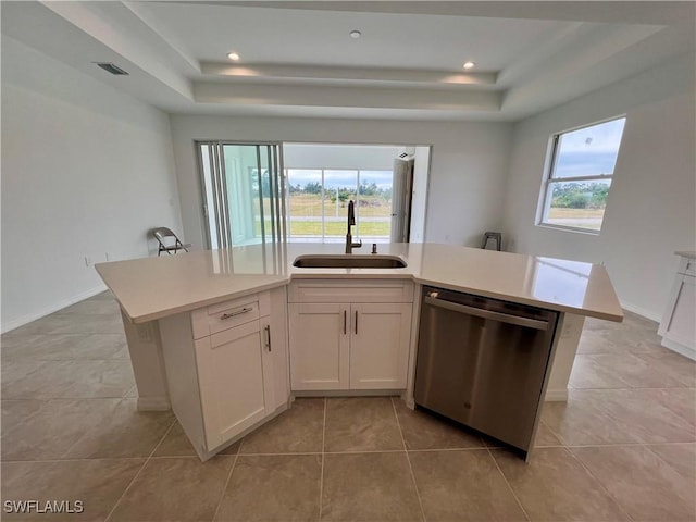 kitchen with a raised ceiling, a kitchen island with sink, sink, and stainless steel dishwasher