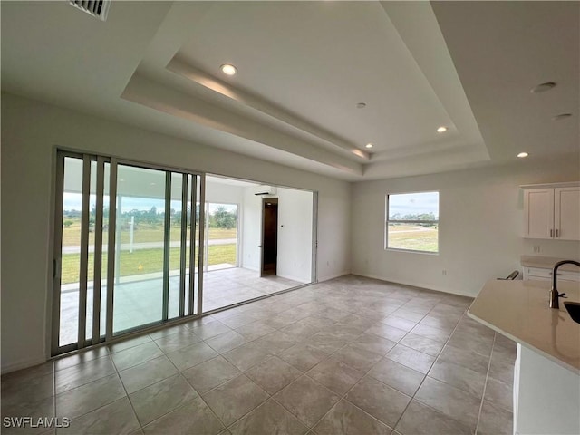 unfurnished living room with a tray ceiling, sink, and light tile patterned floors