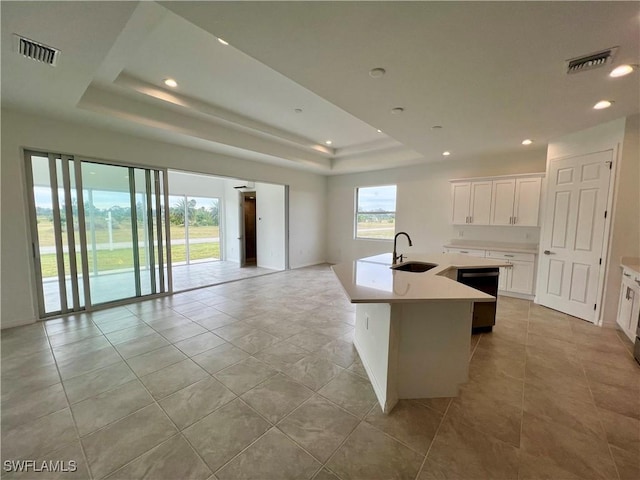 kitchen with a raised ceiling, a kitchen island with sink, sink, light tile patterned floors, and white cabinets