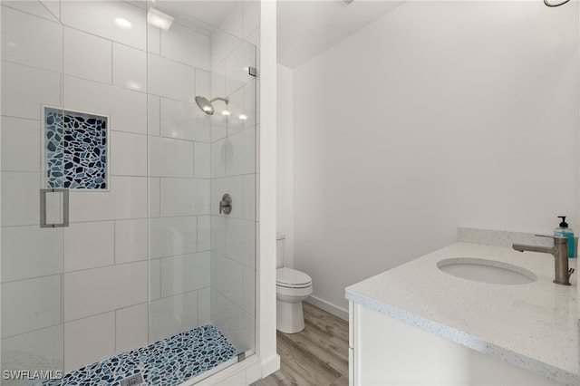 bathroom with toilet, a stall shower, vanity, wood finished floors, and baseboards