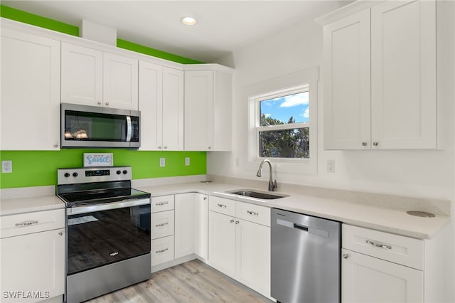 kitchen featuring stainless steel appliances, a sink, white cabinetry, light wood-style floors, and light countertops