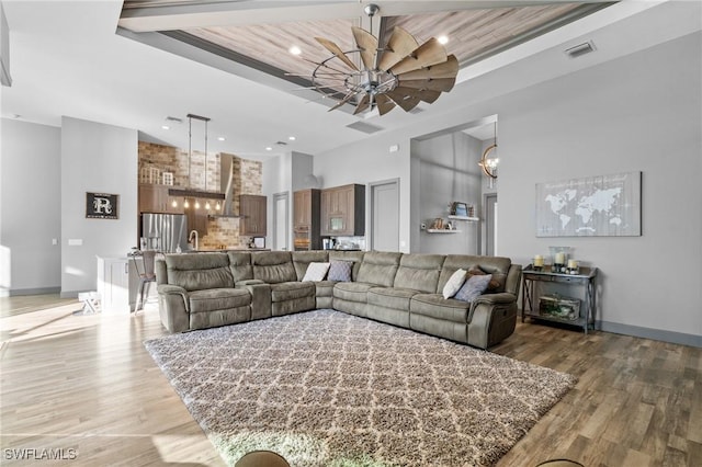 living room with a towering ceiling, wood ceiling, ceiling fan, sink, and wood-type flooring