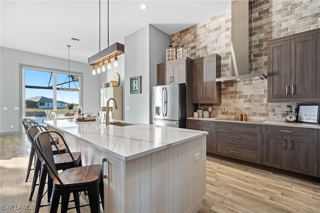 kitchen with stainless steel refrigerator with ice dispenser, black electric stovetop, hanging light fixtures, a breakfast bar area, and an island with sink