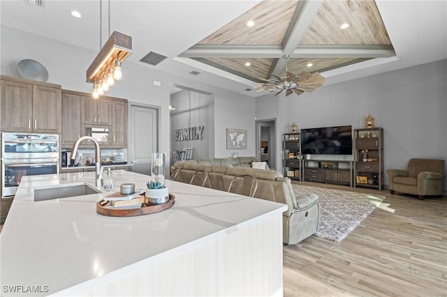 kitchen featuring beam ceiling, coffered ceiling, light stone counters, double oven, and wood ceiling