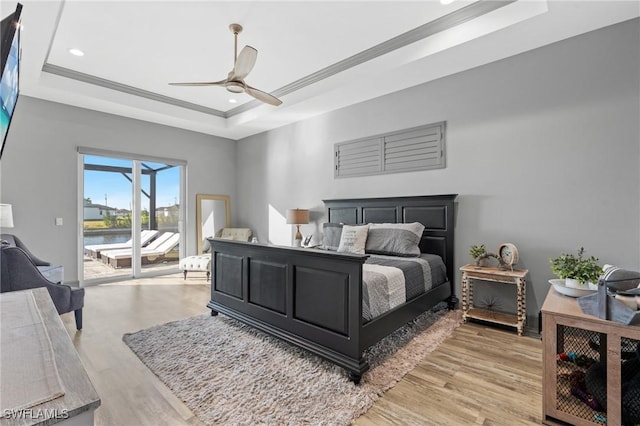 bedroom featuring a raised ceiling, ceiling fan, light wood-type flooring, and access to outside