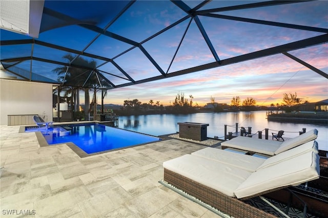 pool at dusk with glass enclosure, a patio area, and a water view