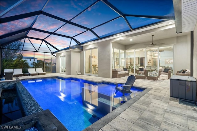 pool at dusk with outdoor lounge area, glass enclosure, ceiling fan, and a patio area