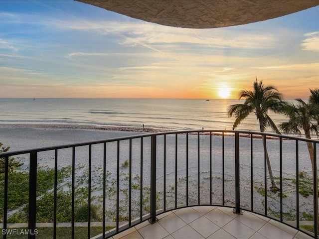 balcony at dusk with a water view and a view of the beach