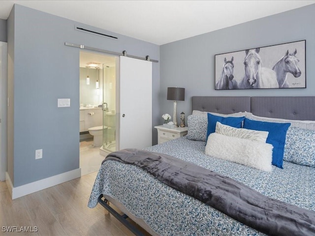 bedroom featuring a barn door, ensuite bath, and light hardwood / wood-style floors