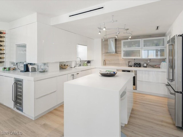 kitchen featuring white cabinetry, high quality fridge, a kitchen island, and wall chimney range hood