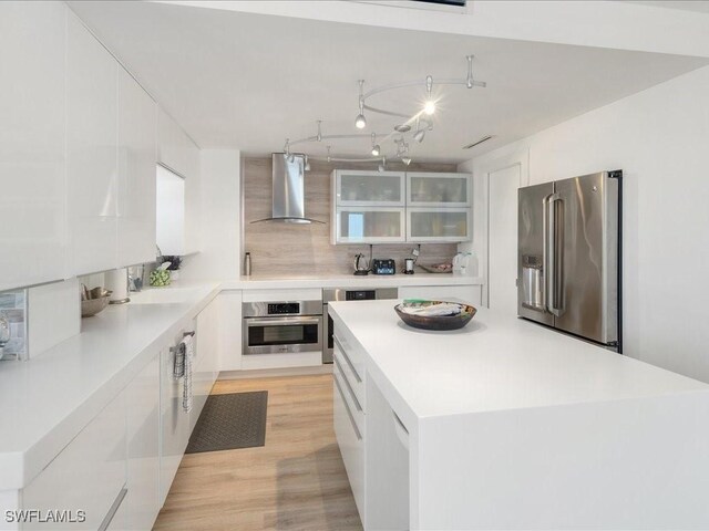 kitchen with a kitchen island, tasteful backsplash, white cabinets, stainless steel appliances, and wall chimney exhaust hood