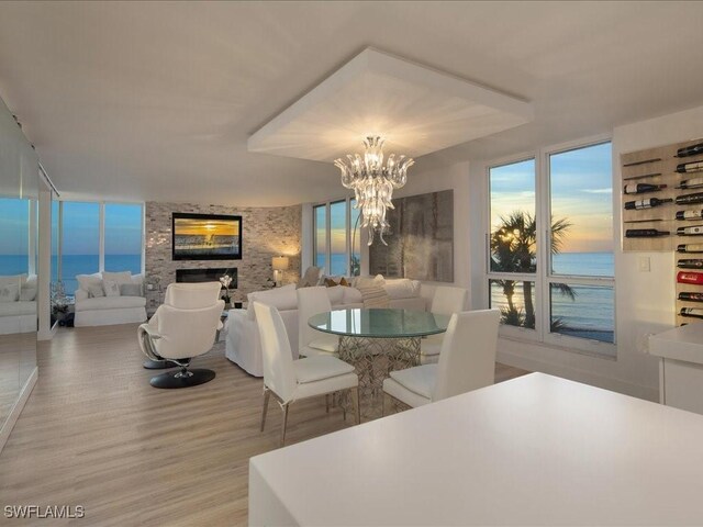 dining space with a water view, a stone fireplace, light wood-type flooring, and a notable chandelier