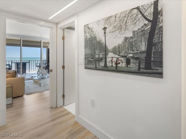 hall with expansive windows, a water view, and light wood-type flooring