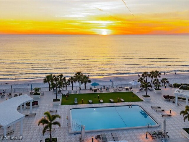 pool at dusk featuring a water view and a patio