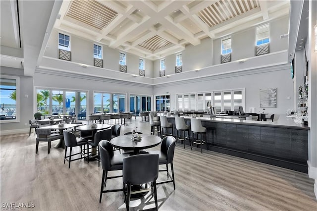 dining room featuring light wood-type flooring, beamed ceiling, a high ceiling, and coffered ceiling