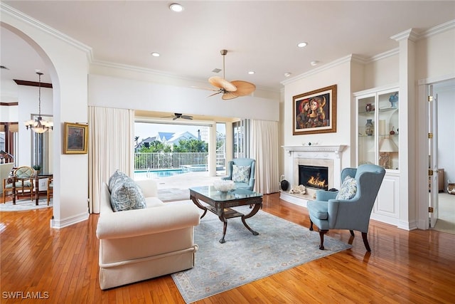 living room featuring ceiling fan with notable chandelier, a premium fireplace, ornamental molding, and light hardwood / wood-style flooring