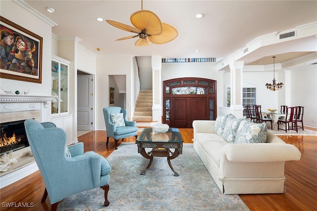 living room with hardwood / wood-style floors, ceiling fan with notable chandelier, ornamental molding, and a premium fireplace