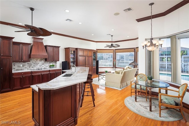 kitchen with backsplash, light hardwood / wood-style floors, black electric cooktop, ceiling fan with notable chandelier, and custom exhaust hood