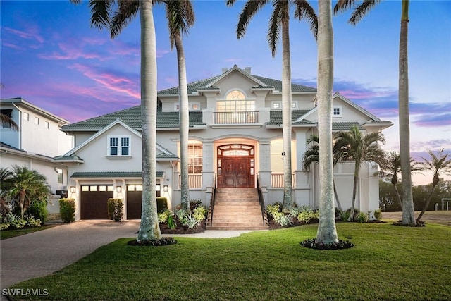 view of front of house with a garage, a balcony, a chimney, decorative driveway, and a front yard