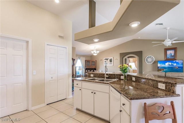 kitchen with lofted ceiling, white cabinets, ceiling fan with notable chandelier, sink, and dark stone countertops