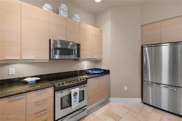 kitchen featuring appliances with stainless steel finishes, light brown cabinets, and dark stone countertops