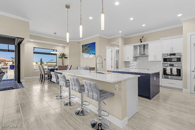 kitchen featuring a center island with sink, wall chimney exhaust hood, white cabinets, and sink