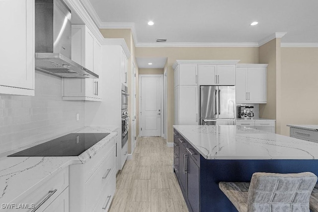 kitchen featuring wall chimney exhaust hood, light stone counters, white cabinetry, and appliances with stainless steel finishes