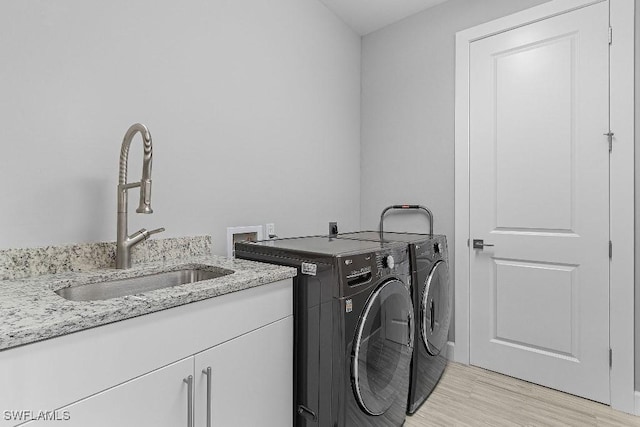 clothes washing area with washer and clothes dryer, cabinets, light wood-type flooring, and sink