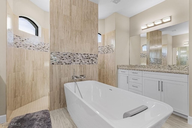 bathroom featuring plus walk in shower, vanity, and tile walls