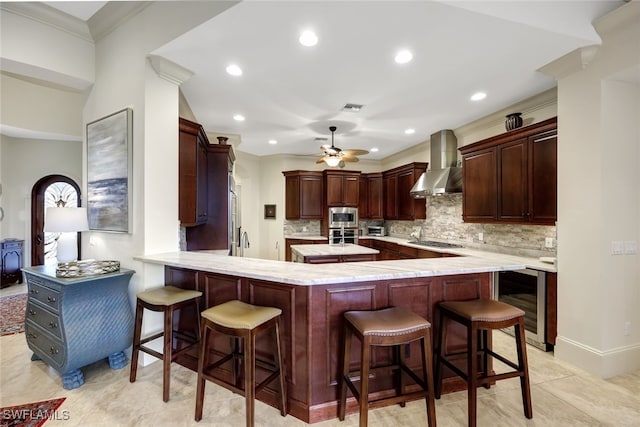 kitchen featuring kitchen peninsula, a kitchen bar, stainless steel appliances, wall chimney exhaust hood, and beverage cooler