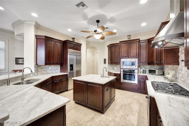 kitchen featuring built in appliances, decorative backsplash, sink, a kitchen island with sink, and range hood