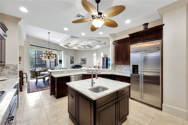 kitchen featuring kitchen peninsula, appliances with stainless steel finishes, a kitchen island with sink, ceiling fan with notable chandelier, and sink