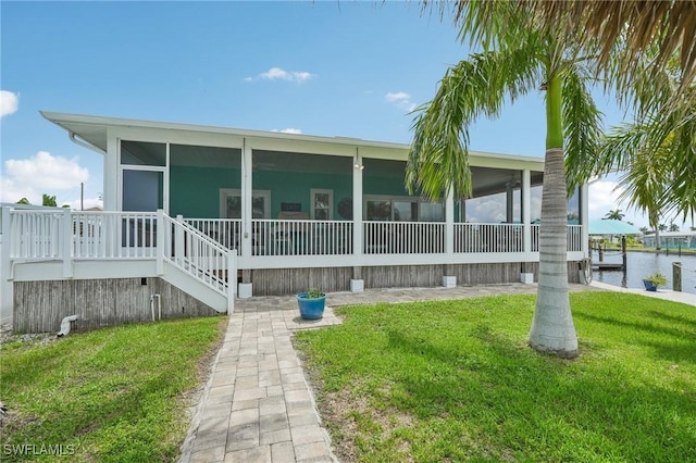 rear view of house with a water view, a lawn, and a sunroom