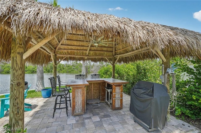 view of patio featuring a gazebo, a grill, a water view, and exterior bar