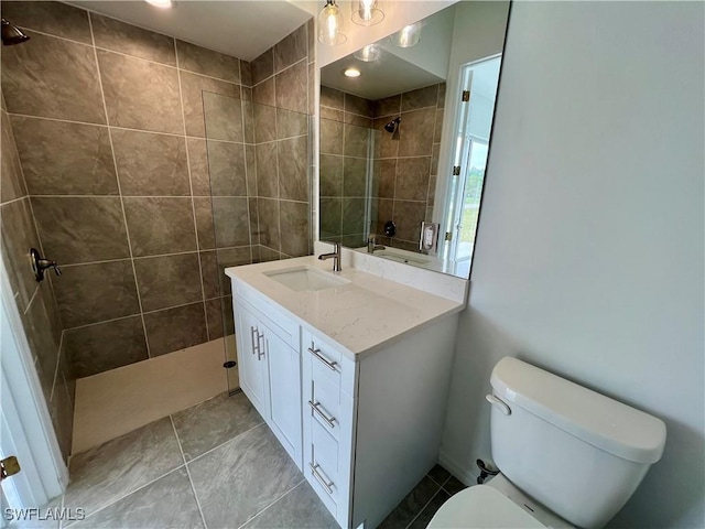 bathroom with a tile shower, tile patterned floors, vanity, and toilet