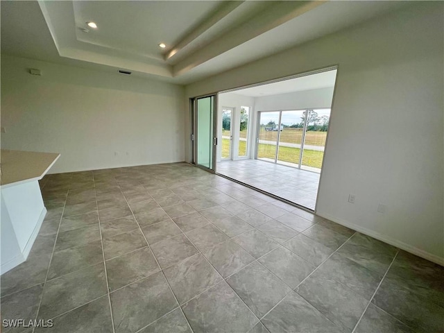 tiled empty room featuring a raised ceiling