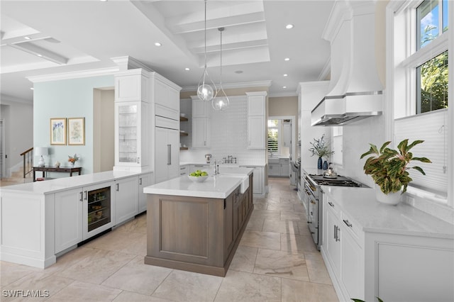 kitchen featuring high end range, custom exhaust hood, beverage cooler, pendant lighting, and white cabinets