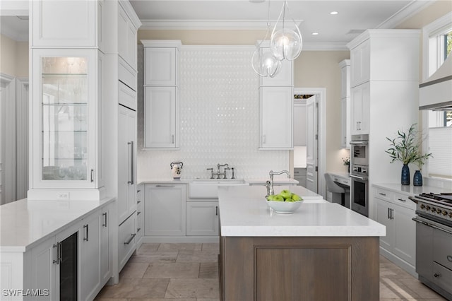 kitchen with sink, hanging light fixtures, ornamental molding, an island with sink, and white cabinetry