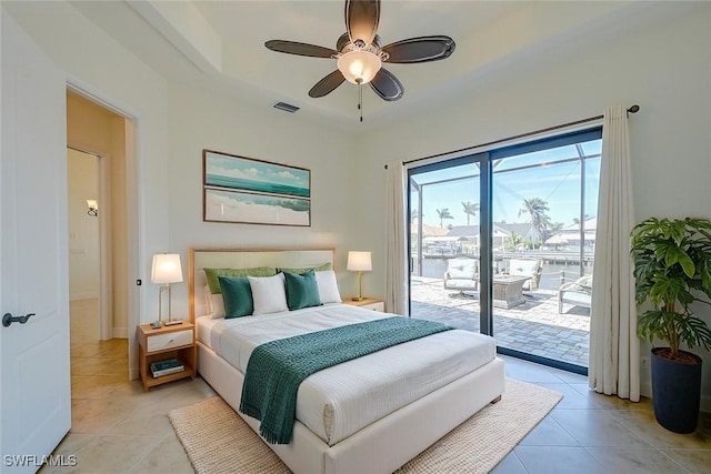 tiled bedroom with ceiling fan, access to outside, a water view, and a tray ceiling