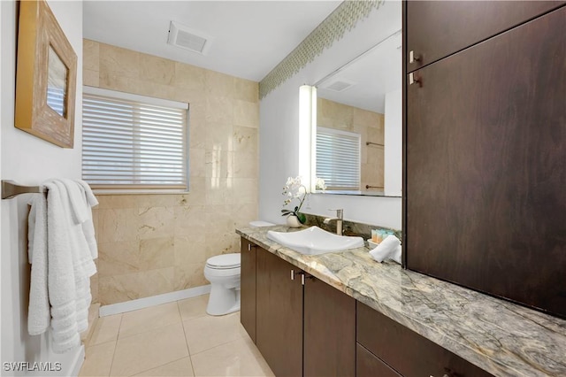 bathroom with toilet, vanity, tile patterned floors, and tile walls