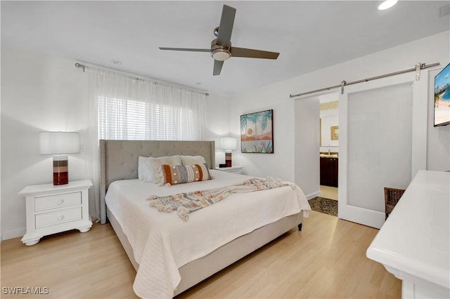 bedroom featuring a barn door, ceiling fan, ensuite bath, and light wood-type flooring